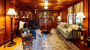 A traditional room with wooden paneling, a large wooden cabinet, a sofa, a chair, a small table, and a floor lamp. - Home Near Hiking Biking w Hottub 6 Bedrooms (Bennington)