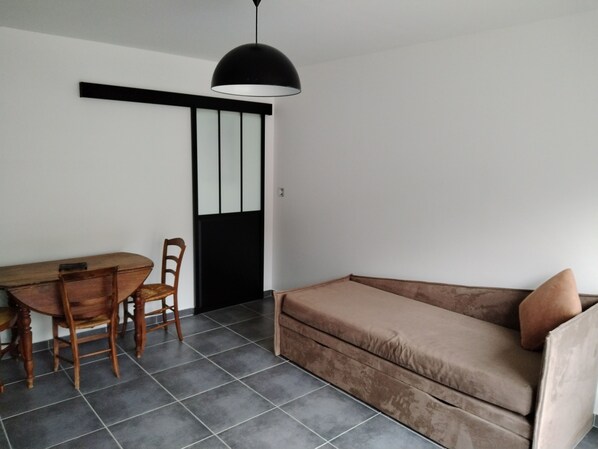 A minimalist room with a sofa, a dining table with chairs, and a black pendant light. - ART on the ground floor and terrace  (Beautheil-Saints)