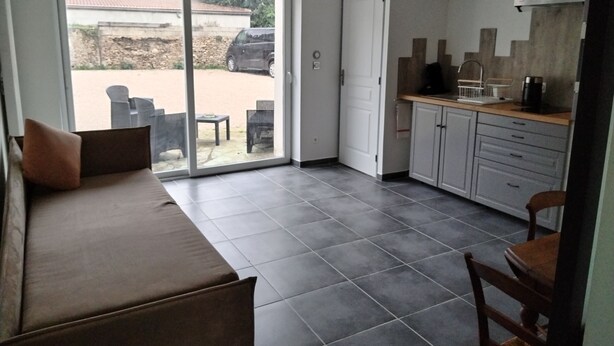 A modern kitchen with grey cabinets and a black pendant light, a dining area with a brown sofa and chairs, and a sliding glass door leading to an outdoor patio with a car and chairs visible. - ART on the ground floor and terrace  (Beautheil-Saints)