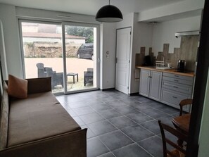 A modern kitchen with grey cabinets and a black pendant light, a dining area with a brown sofa and chairs, and a sliding glass door leading to an outdoor patio with a car and chairs visible. - ART on the ground floor and terrace  (Beautheil-Saints)