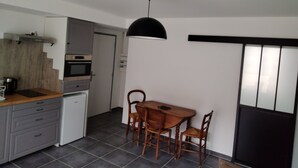 A compact kitchen with a dining table and chairs, a white refrigerator, and a black pendant light. - ART on the ground floor and terrace  (Beautheil-Saints)