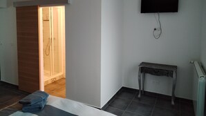 A hotel room with a shower, a bed, a TV mounted on the wall, and a small table. - ART on the ground floor and terrace  (Beautheil-Saints)