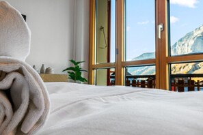 A neatly made bed with a towel, a plant, and a window with a mountain view. - Beautiful, centrally located apartment in Leukerbad (Leukerbad)