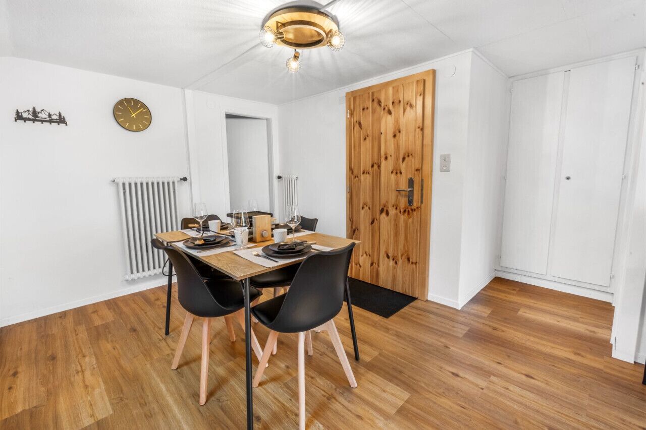 Un'area pranzo con un tavolo in legno apparecchiato per quattro persone, sedie nere, un termosifone bianco e una porta in legno.