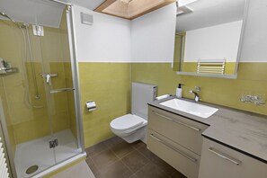 A modern bathroom with a glass shower enclosure, a white toilet, and a beige vanity with a sink. - Beautiful, centrally located apartment in Leukerbad (Leukerbad)