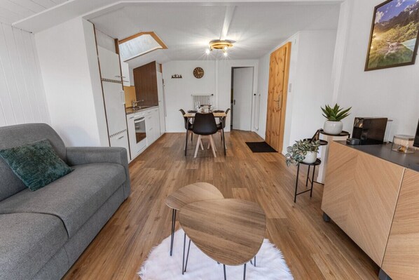A modern living room with a grey sofa, a wooden dining table, and a kitchen area with wooden cabinets and a white countertop. - Beautiful, centrally located apartment in Leukerbad (Leukerbad)