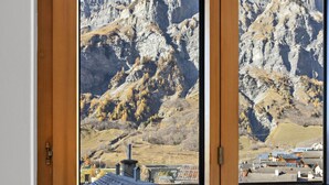 A view through a window of a mountainous landscape with a village below. - Beautiful central apartment in Leukerbad (Leukerbad)