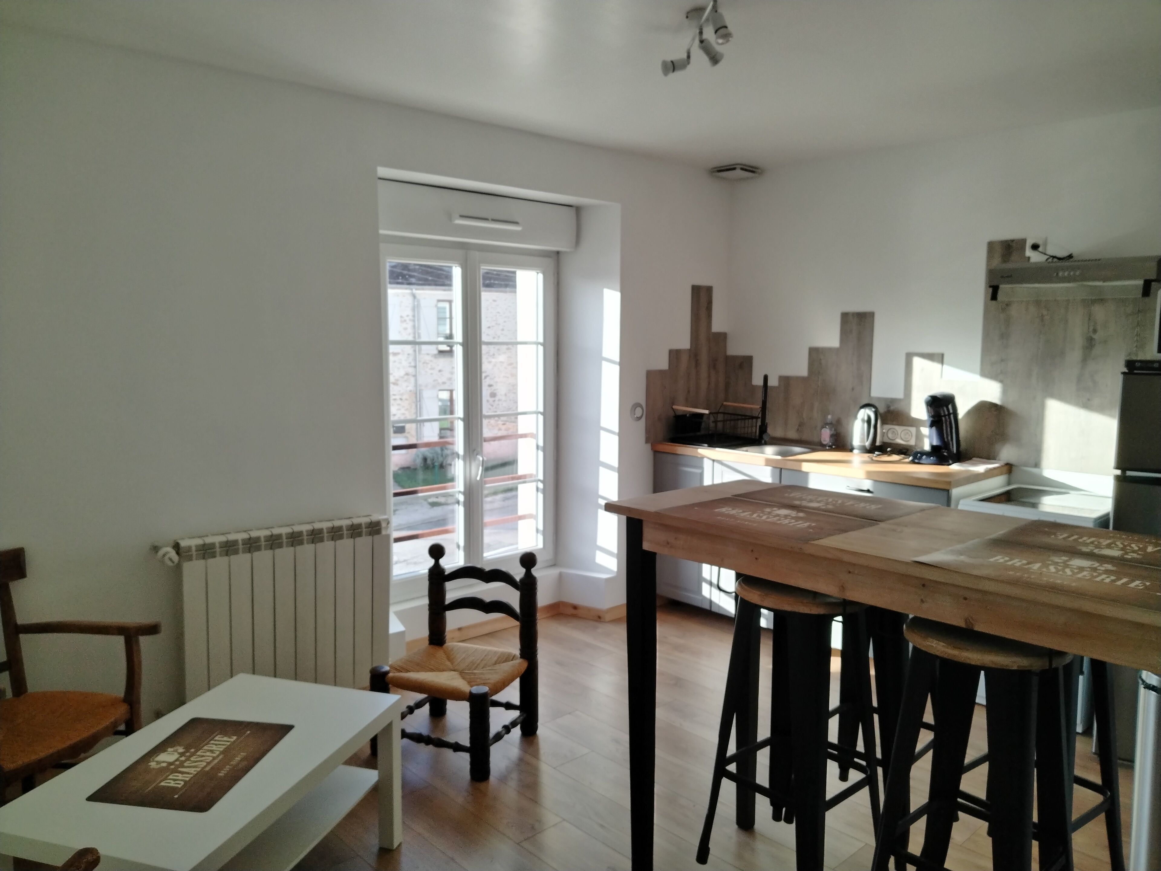 A modern kitchen with a wooden table, bar stools, and a view of the street through a glass door. - L' ART Appart from 2 to 4 pers, 7 min from coulommiers, 25 min from Disneyland Paris (Beautheil-Saints)