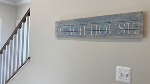 A wall-mounted sign that reads "Welcome to our BEACH HOUSE" with a staircase in the background. - Spacious, New 4-bdrm townhome in charming Lewes, walk or bike to town & beaches! (Lewes)