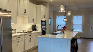 A modern kitchen with white cabinets, stainless steel appliances, and a central island. - Spacious, New 4-bdrm townhome in charming Lewes, walk or bike to town & beaches! (Lewes)