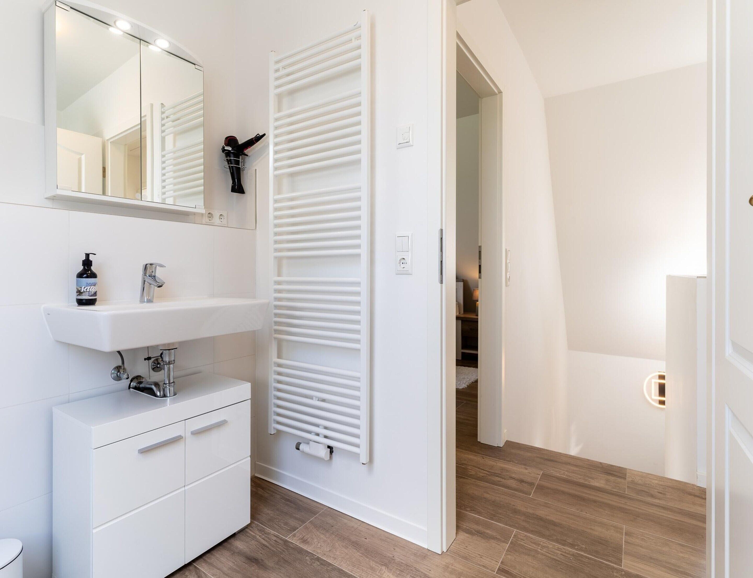 A modern bathroom with a white vanity, a mirror, a towel rack, and a radiator.