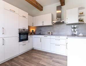 A modern kitchen with white cabinetry, a built-in oven, a stainless steel range hood, and a wooden floor. - Ferienhaus in Tating (Tating)