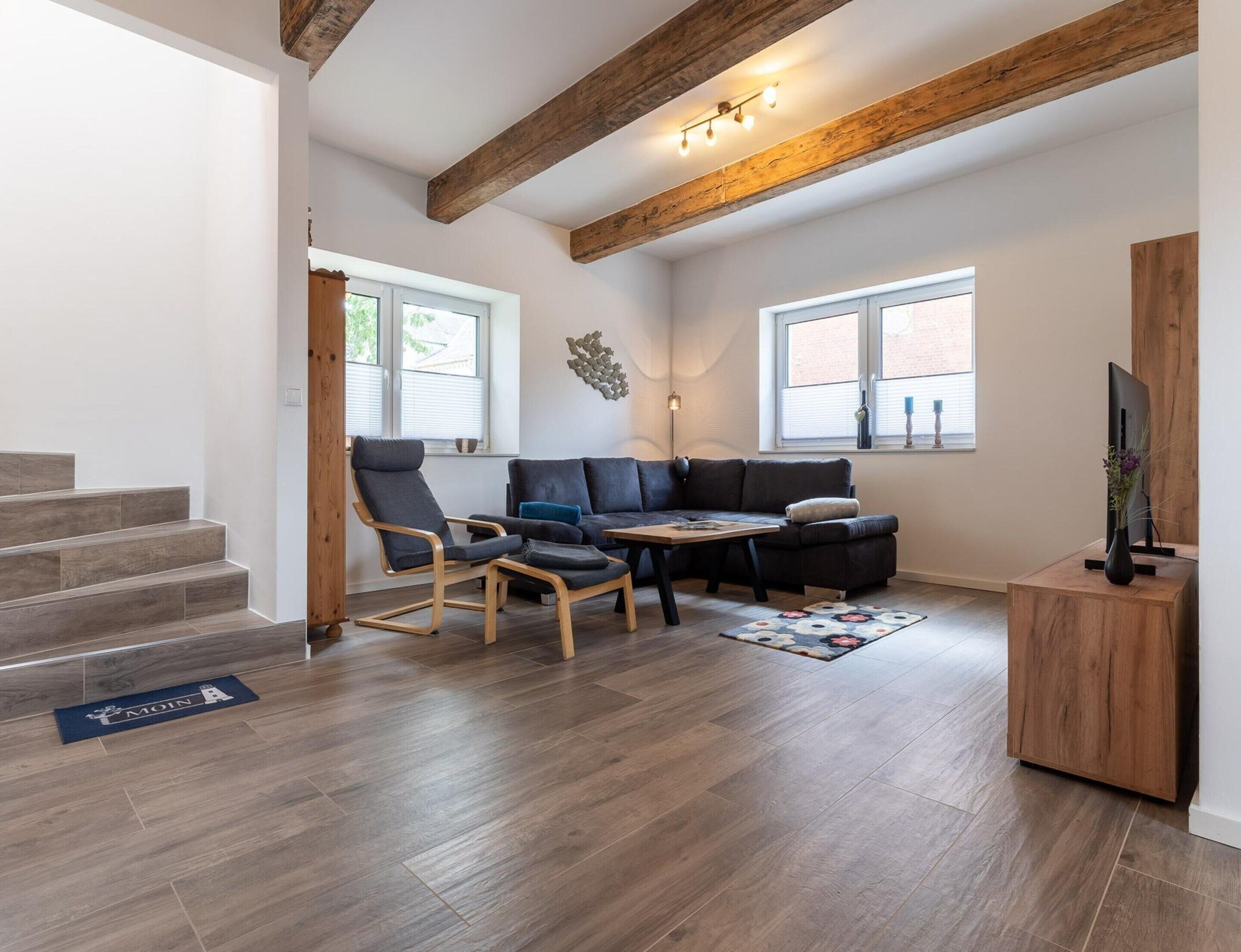 Una sala de estar moderna con un sofá modular, dos mecedoras, una mesa de centro y un televisor sobre un soporte de madera.