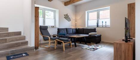 Una sala de estar moderna con un sofá modular, dos mecedoras, una mesa de centro y un televisor sobre un soporte de madera.