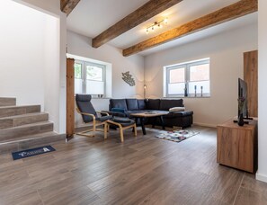A modern living room with a sectional sofa, two rocking chairs, a coffee table, and a TV on a wooden stand. - Ferienhaus in Tating (Tating)