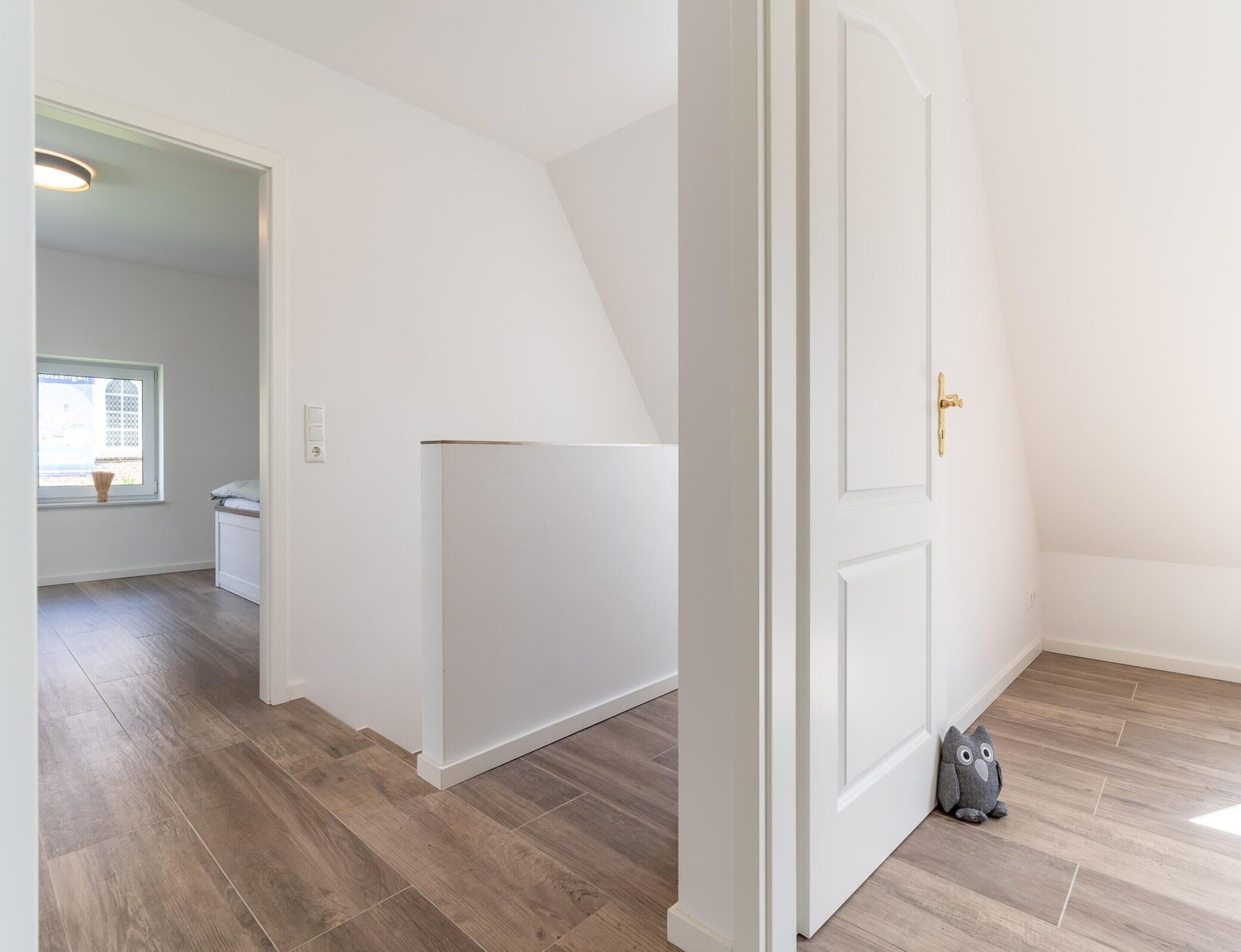 A hallway with a white door, a window with blinds, and a grey owl plush toy on the floor.