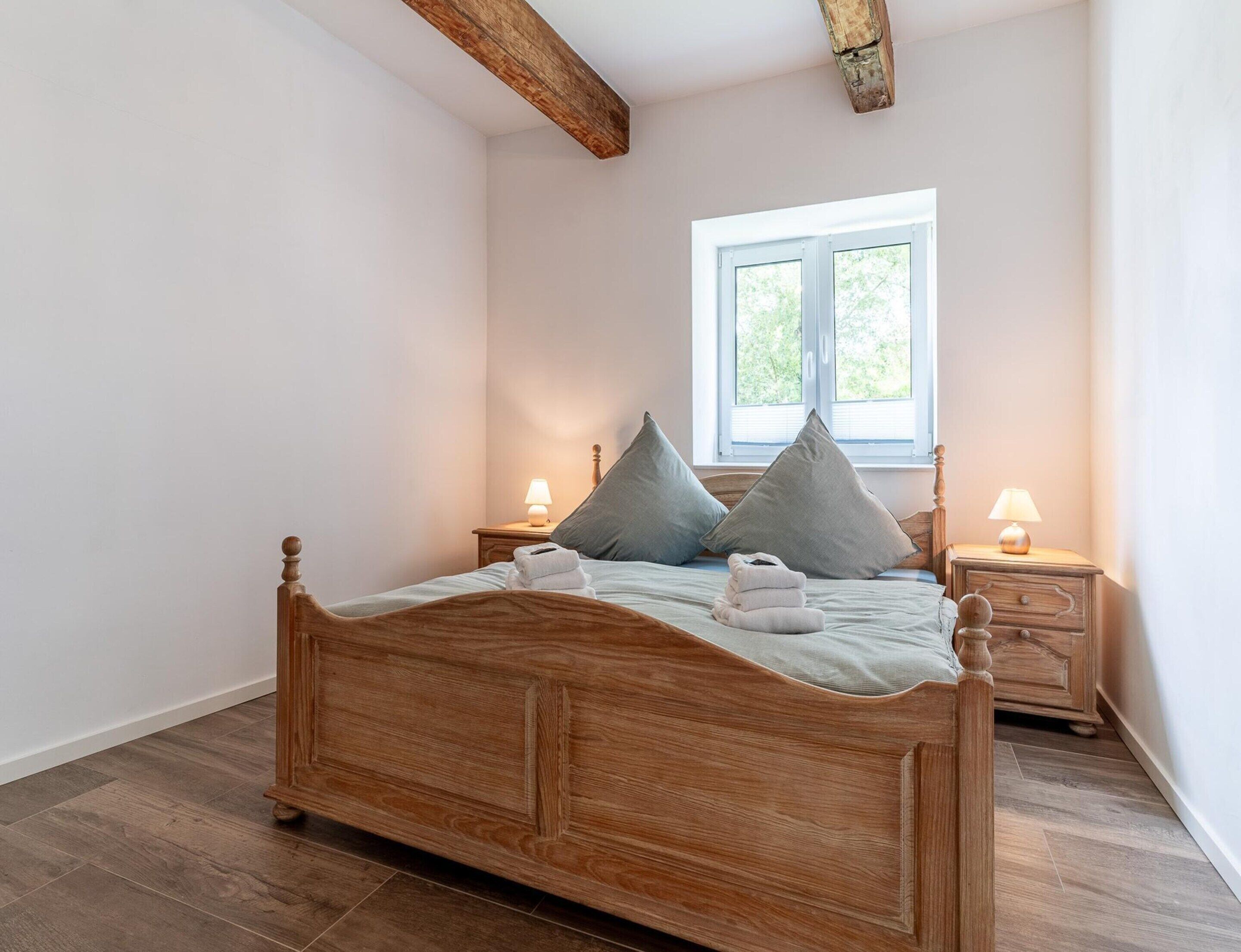 Un lit en bois avec une tête de lit, deux tables de chevet avec des lampes et une fenêtre avec des stores.