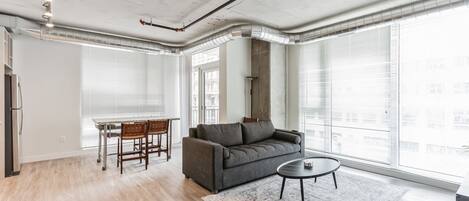 Amplia sala de estar con un sofá gris, una mesa de centro redonda y un comedor con mesa y sillas.