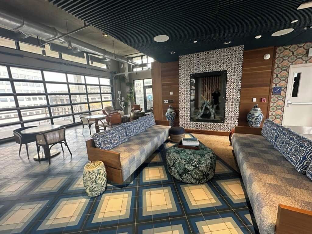 A modern lounge area with a large window, patterned floor, and seating arrangements.