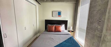 Un dormitorio con una cama, ventilador de techo, ventana con persianas y una obra de arte colgada en la pared.