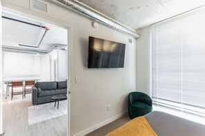 Una sala moderna con un sofá gris, un sillón verde y un televisor de pantalla plana montado en la pared.