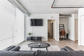 Ein modernes Wohnzimmer mit einem flachbildfernseher an der Wand, einem schwarzen Konsolentisch mit Pflanze, einem runden Couchtisch und einem grauen Sofa.