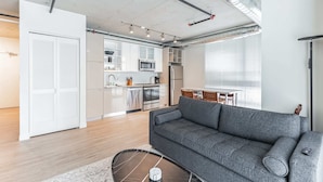 Un apartamento moderno con un sofá gris, una cocina con armarios blancos y una zona de comedor.
