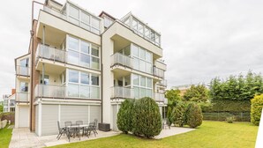 Ein mehrstöckiges Wohngebäude mit Balkonen, einer Terrasse mit Gartenmöbeln und einem gepflegten Rasen.