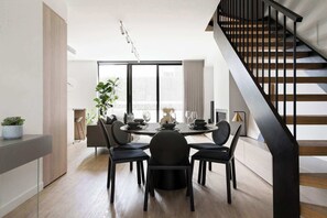 A modern dining area with a round table, black chairs, and a staircase with wooden steps and black railings.