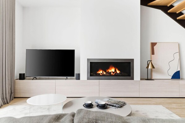 A modern living room with a flat-screen TV, a fireplace, and a coffee table with magazines.