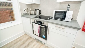 A modern kitchen with white cabinets, a built-in oven, a microwave, and a kettle.