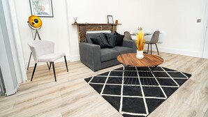 A modern living room with a grey sofa, a round wooden coffee table, and a black and white rug.