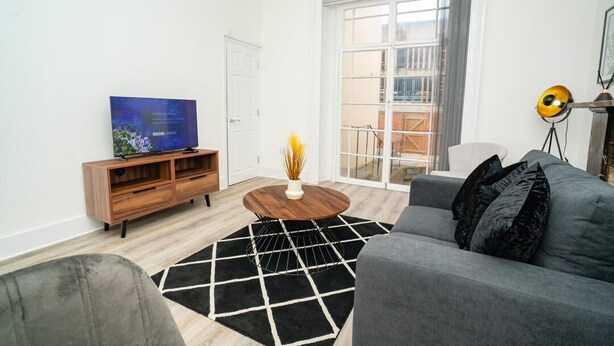 A modern living room with a flat-screen TV, a wooden TV stand, a round coffee table, a gray sofa, and a black and white rug.