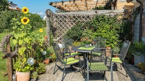 Une terrasse avec une table ronde et quatre chaises, entourée de plantes en pot et d’une clôture en bois.