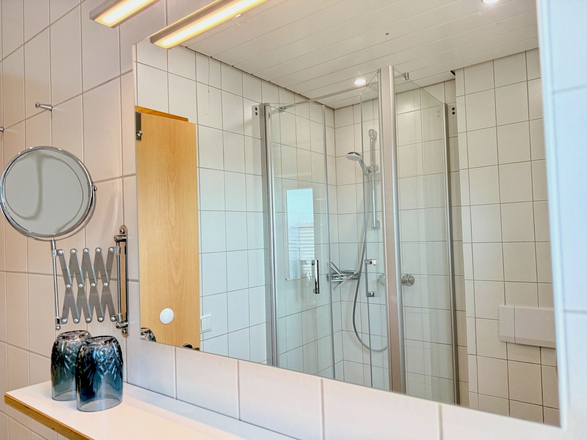 Un baño moderno con ducha acristalada, un espejo redondo y un mueble de tocador de madera.