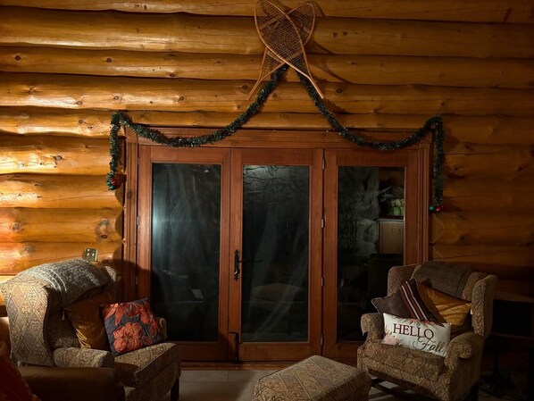 Interior de una cabaña de troncos con una puerta de madera, dos sillones y un cartel que dice 'HELLO Fall'.