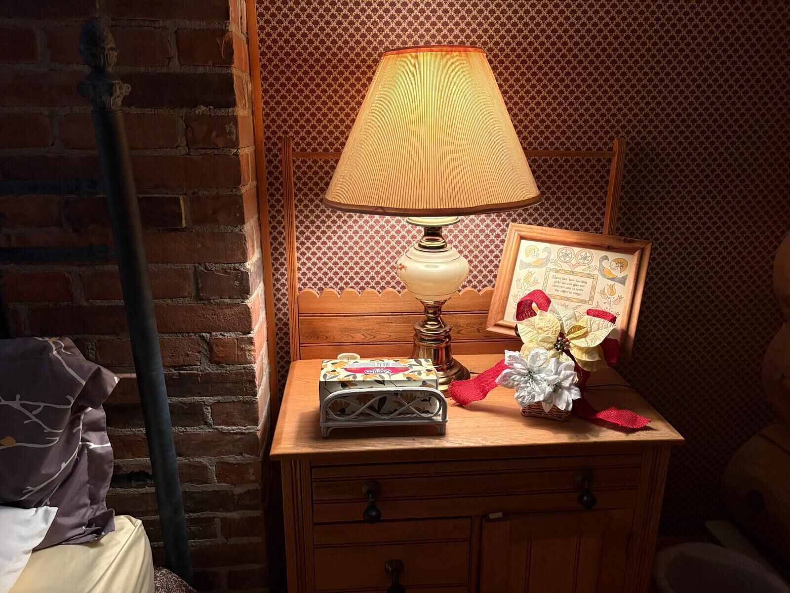 A wooden nightstand with a lamp, a framed picture, and a small basket with a tissue box.