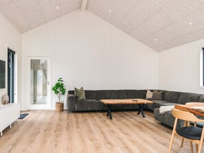 A spacious living room with a large grey sectional sofa, a wooden coffee table, and a dining area with a wooden table and chairs.