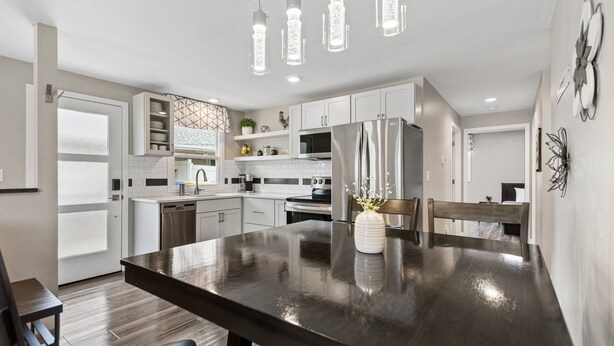 A modern kitchen with white cabinetry, stainless steel appliances, and a dark wooden dining table. - 1218-1220 Lambeau Luxe (Green Bay)