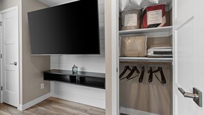 A modern room with a mounted TV, a built-in shelf, a coat rack, and a closet with hanging clothes. - 1218-1220 Lambeau Luxe (Green Bay)