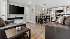 A modern living room with a flat-screen TV, leather sofas, a dining area with a table and chairs, and a kitchen with stainless steel appliances. - 1218-1220 Lambeau Luxe (Green Bay)