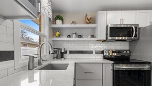 A modern kitchen with white cabinets, a stainless steel stove, a microwave, and a black oven. - 1218-1220 Lambeau Luxe (Green Bay)