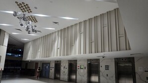 Un vestíbulo amplio con diseño moderno, que presenta suelo de mármol, varios ascensores y una lámpara decorativa en el techo.