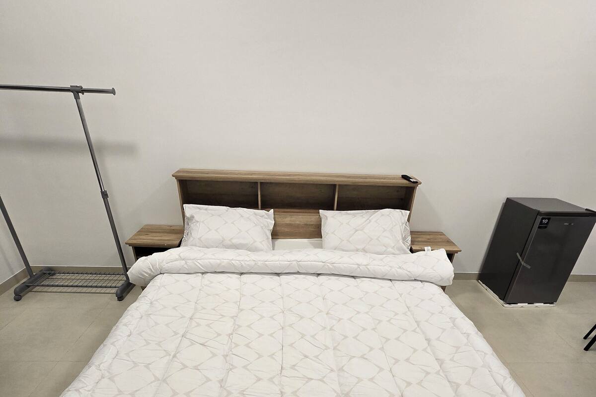 A neatly made bed with a quilted white cover, a wooden headboard, and a small bedside table with a remote control.