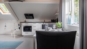 A modern kitchen with white cabinetry, a black chair, a dining table with two wine glasses, and a potted plant. - Studio in Kamperland With Terrace (Kamperland)