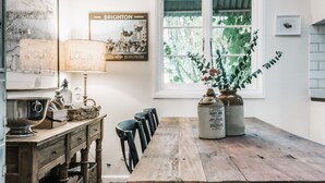 A rustic kitchen with a wooden table, vintage lamps, and a window with greenery outside. - Lola Cottage - Your Charming Retreat in the Heart of Adaminaby (Adaminaby)
