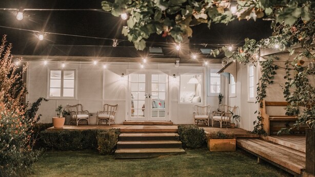 A cozy outdoor seating area with wooden benches and chairs, surrounded by a well-maintained lawn and decorative string lights. - Lola Cottage - Your Charming Retreat in the Heart of Adaminaby (Adaminaby)
