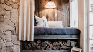 A cozy room with a stone wall, a wooden bench with cushions, and a log storage area. - Lola Cottage - Your Charming Retreat in the Heart of Adaminaby (Adaminaby)