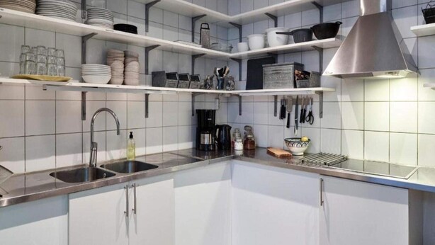 A modern kitchen with white cabinets, stainless steel countertops, and a variety of kitchenware on shelves.