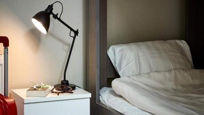 A neatly made bed with white bedding, a bedside table with a lamp, and a red suitcase.